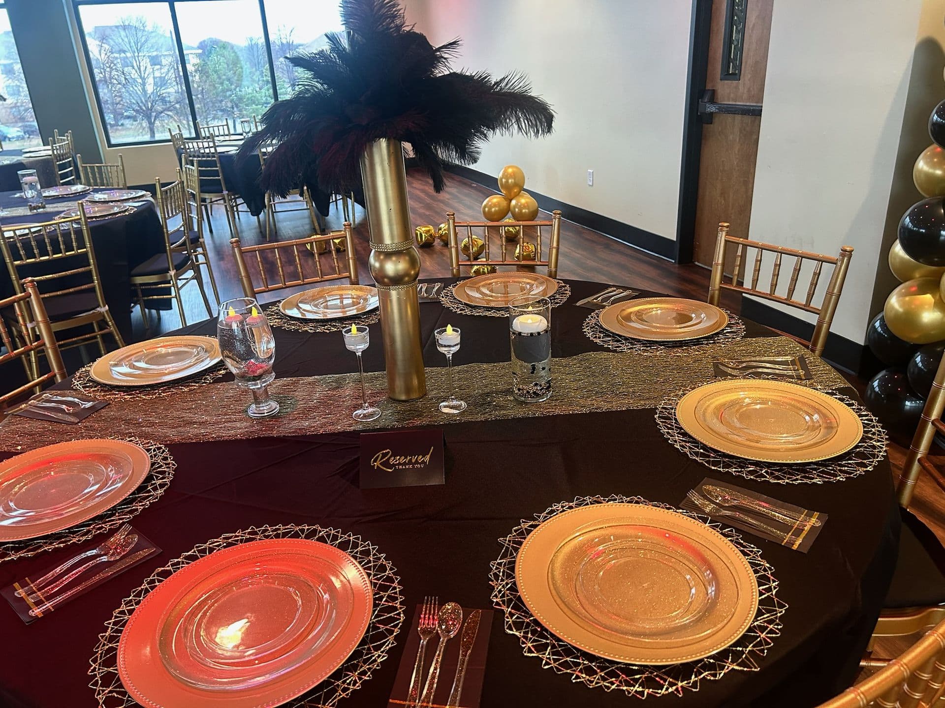 Birthday party table with black-and-gold place settings and feather centerpiece