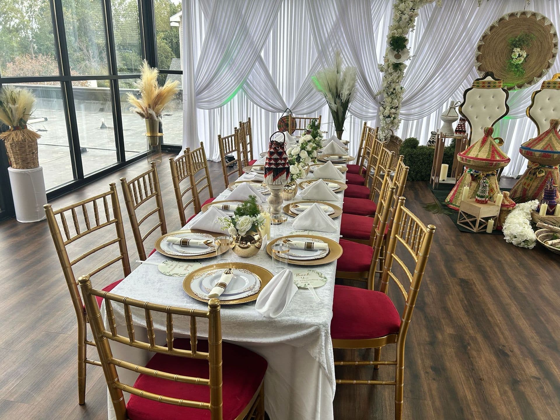 Long banquet table with gold chargers and red chairs at a cultural wedding celebration