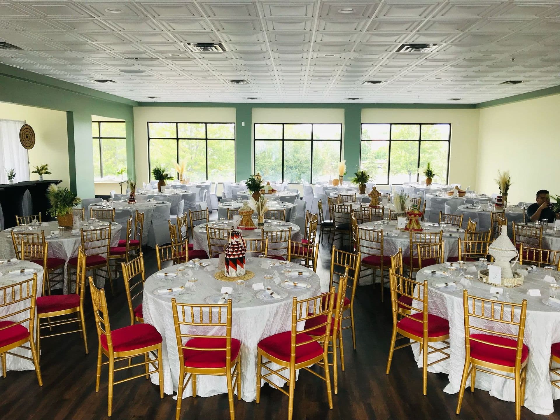 Reception set with round tables and gold chairs in the Green House Grove room at BB's Events & Restaurant