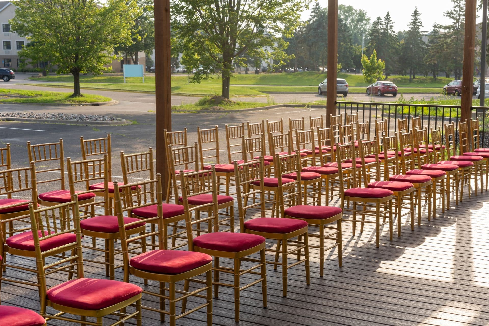 Outdoor ceremony seating with red-cushioned gold chairs under The Pergola